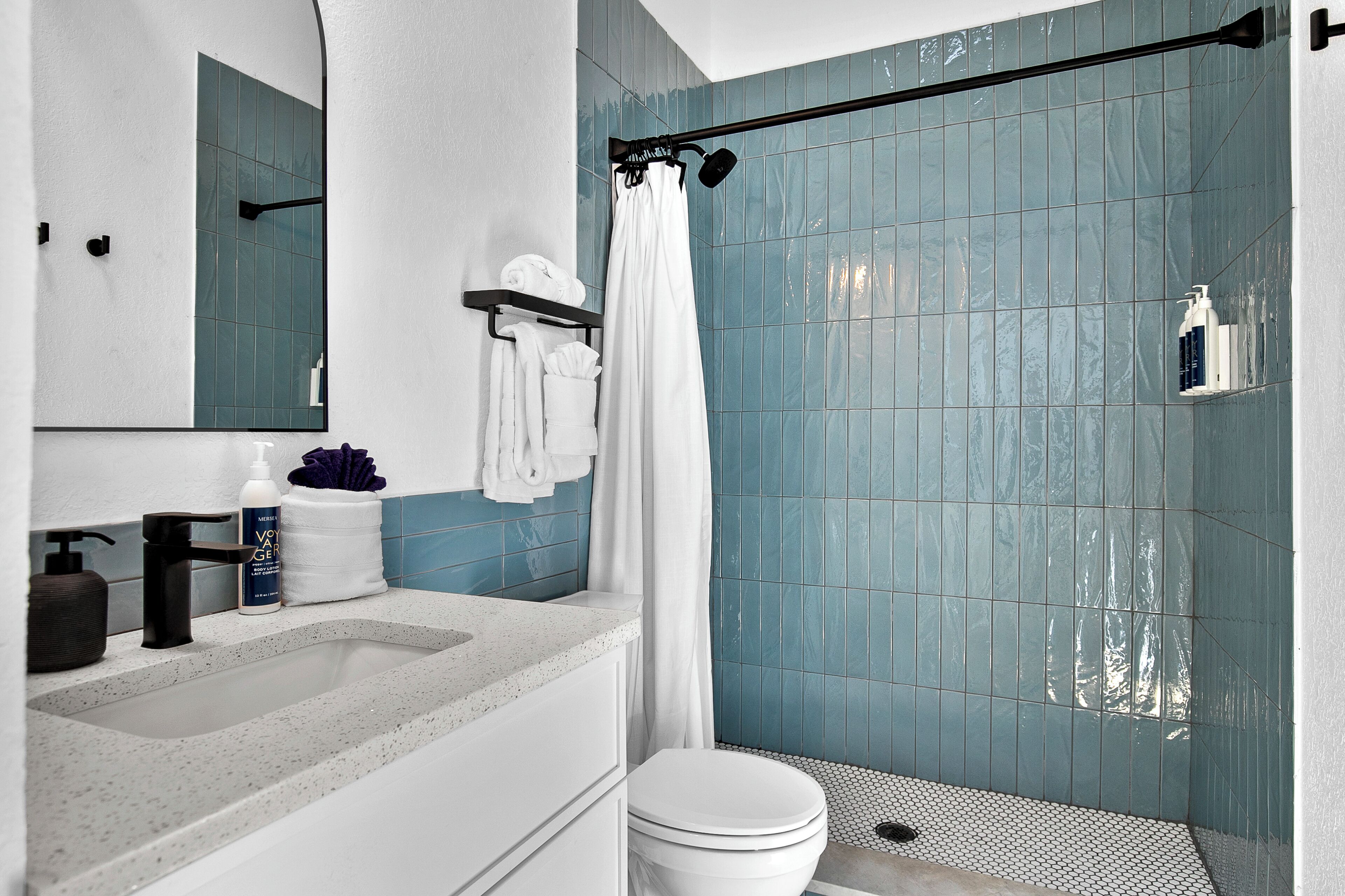 A bathroom with a white sink, a toilet, and a shower with blue tiles.