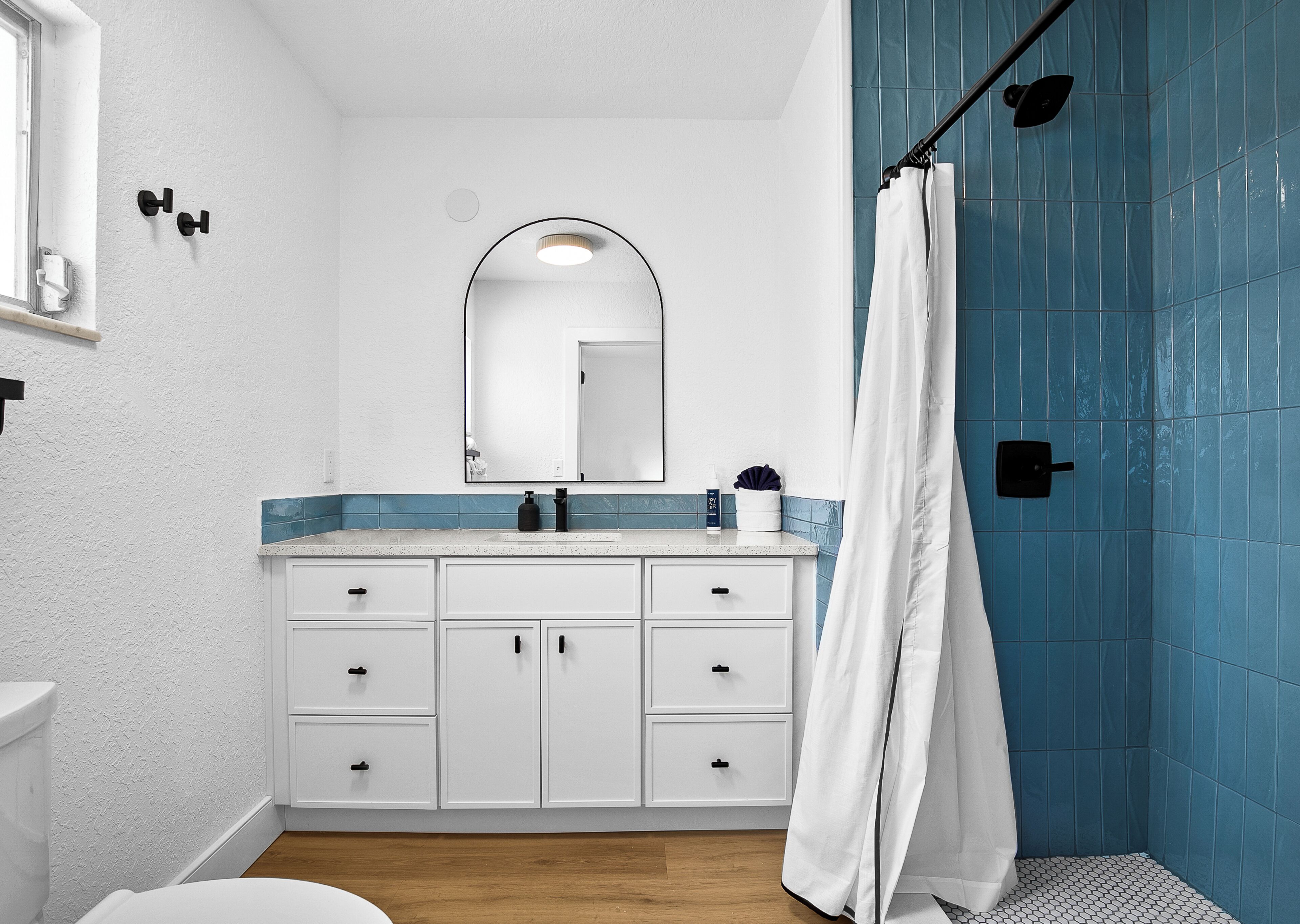 A bathroom with a white vanity, a mirror, a shower with blue tiles, and a white toilet.