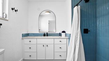 A bathroom with a white vanity, a mirror, a shower with blue tiles, and a white toilet.