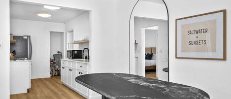A modern kitchen with white cabinetry, a black countertop, and a framed sign on the wall.