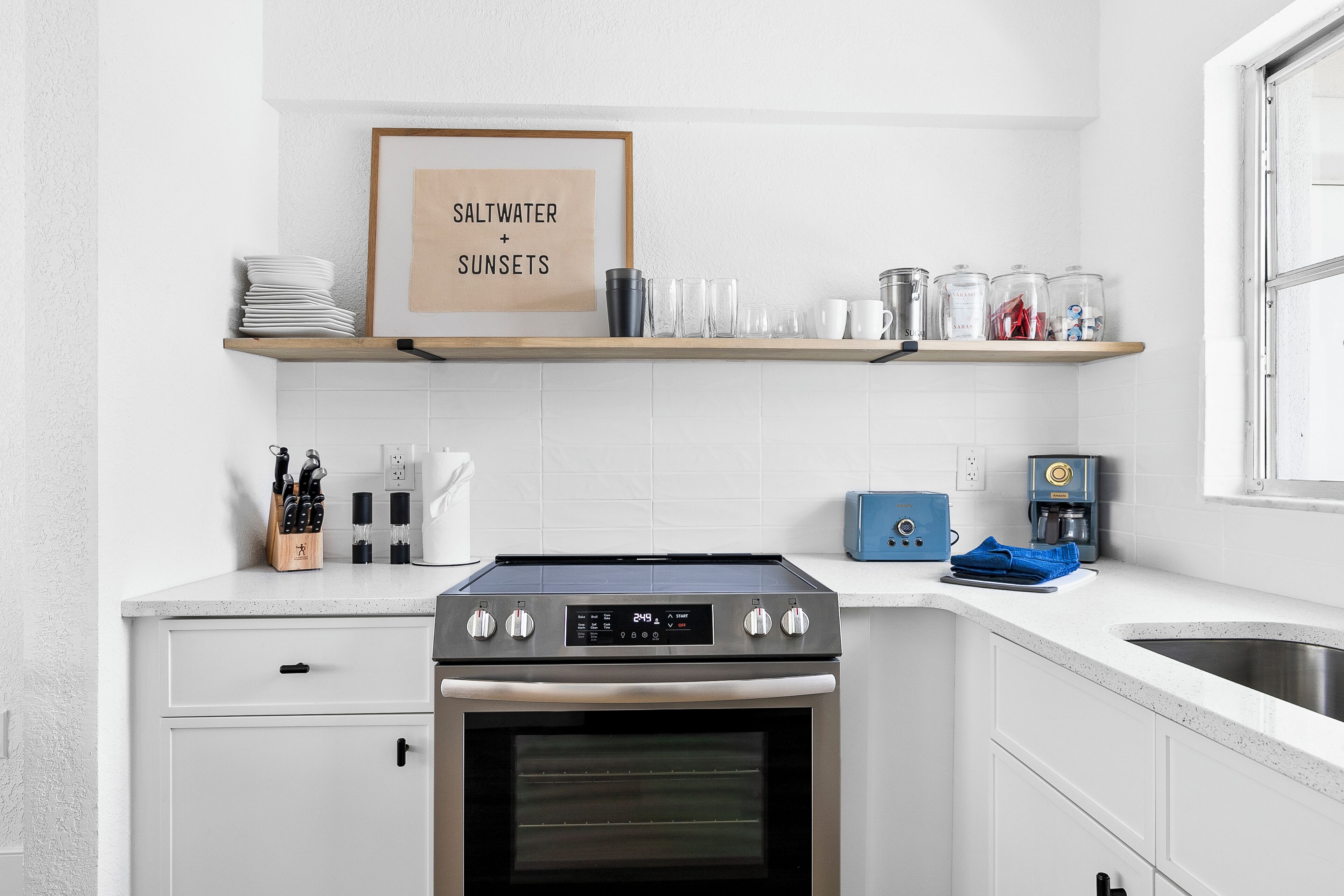 Une cuisine moderne équipée d’un four encastré, d’une machine à café et d’une affiche encadrée au-dessus du plan de travail.
