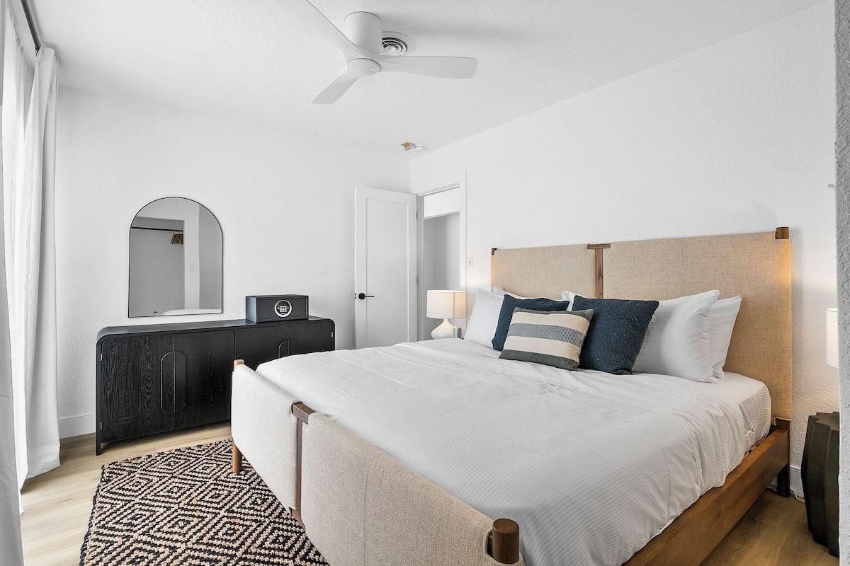 A modern bedroom with a bed, a ceiling fan, a dresser, and a mirror.