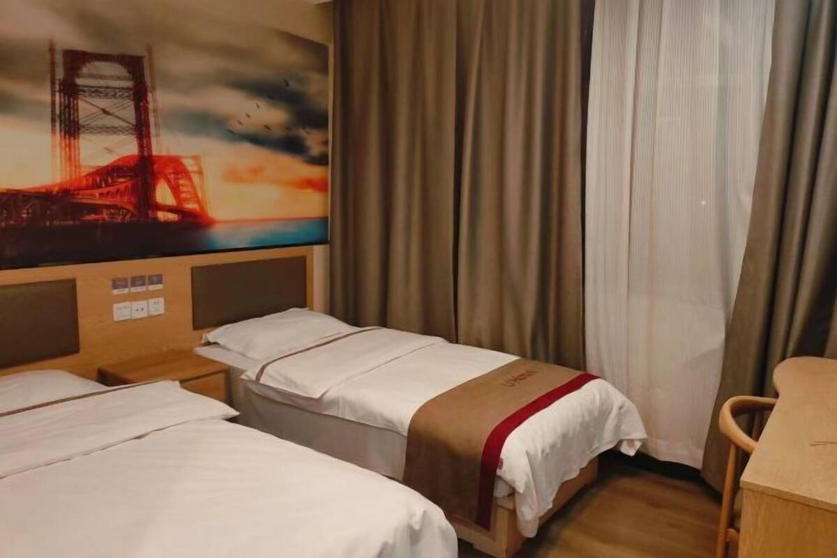 A hotel room with two beds, a desk, and a painting of a bridge.