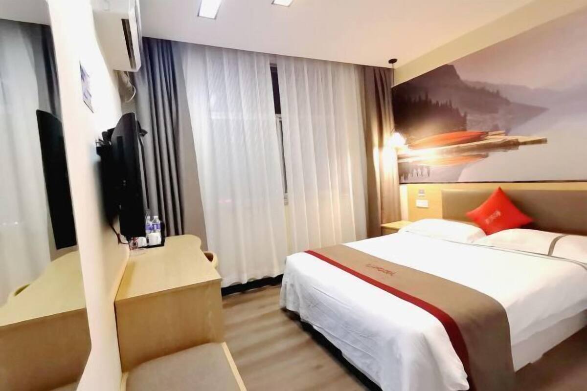 A hotel room with a bed, a desk, a TV, and a painting on the wall.