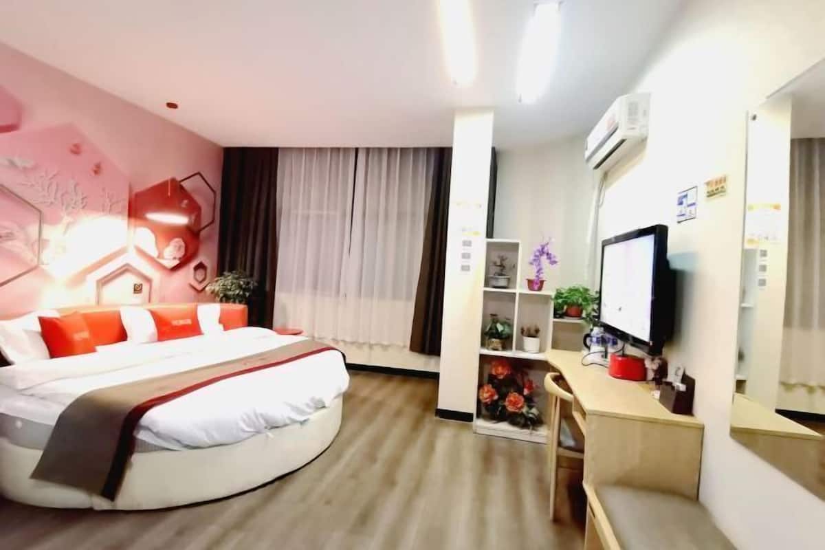 A hotel room with a bed, a desk, a TV, and a bookshelf.