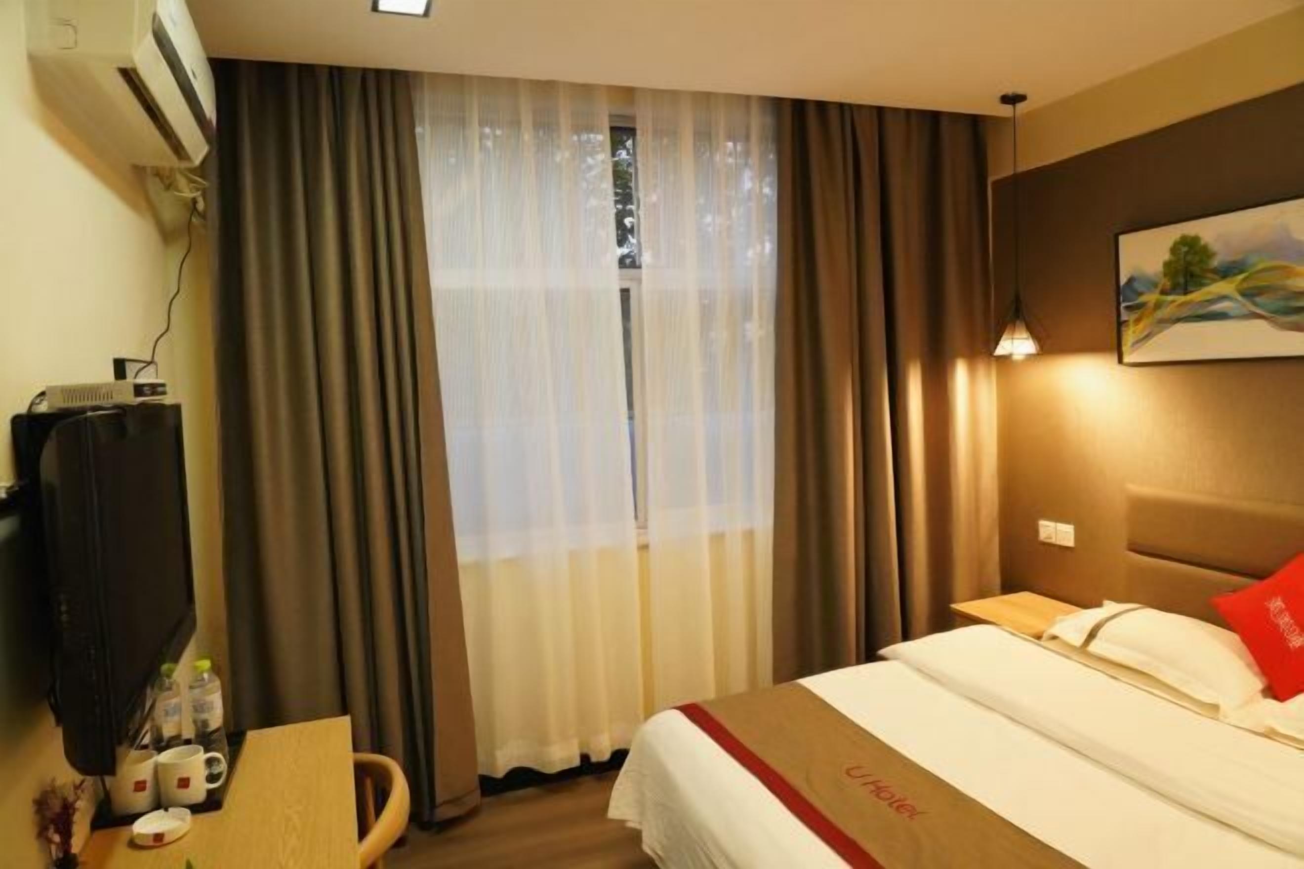 Una habitación de hotel con cama, escritorio con televisor y ventana con cortinas.