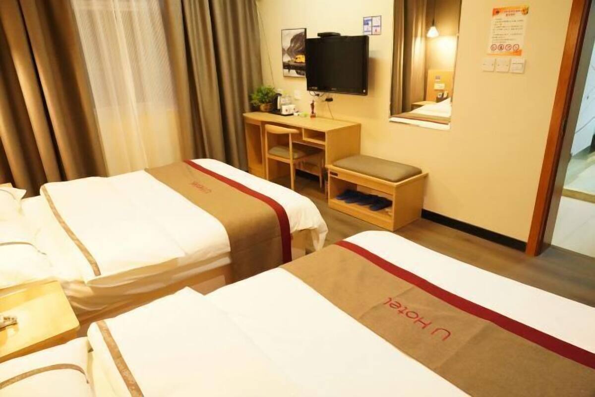 A hotel room with two beds, a desk, a television, and a mirror.