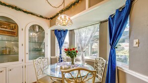 A dining area with a glass table surrounded by white chairs, a chandelier, and blue curtains. - 9 Mi to Dtwn: Spacious Retreat in Corpus Christi! (Corpus Christi)