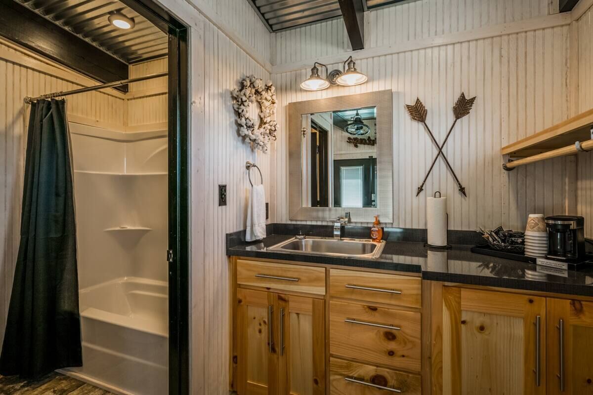 A bathroom with a shower, a sink with a mirror, wooden cabinets, and a towel rack.