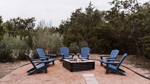 Een vuurkuil met vier Adirondack-stoelen eromheen, gelegen in een zandrijk buitengebied.
