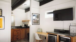 Een compacte hotelkamer met kitchenette, een bed, bureau met stoel, flatscreen-tv en een lijst aan de muur.