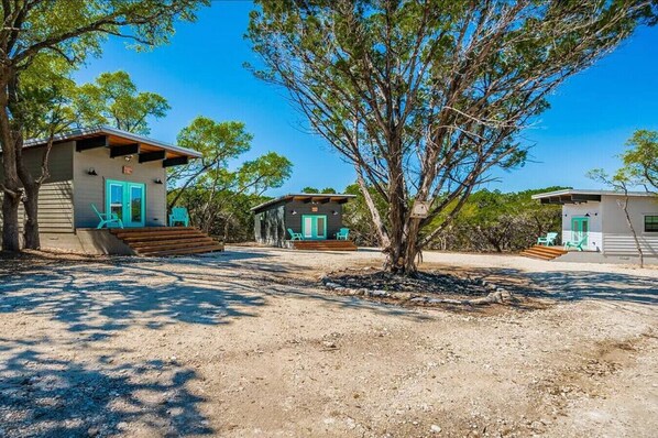 A property with multiple cabins, each featuring a distinct architectural style, surrounded by natural vegetation and a clear sky.