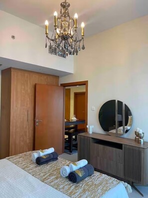 A hotel room with a bed, a wooden wardrobe, a desk with a mirror, and a chandelier.