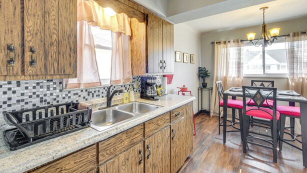 A kitchen with wooden cabinets, a granite countertop, a sink, and a dining area with a table and chairs. - 8 Mi to Dtwn Cleveland: Quiet Home w/ Fenced Yard (Garfield Heights)