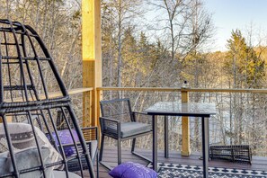 Eine Holzterrasse mit Korbstühlen und einem Tisch mit Blick auf ein bewaldetes Gebiet.