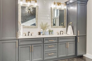 Ein modernes Badezimmer mit grauem Waschtisch, zwei Spiegeln mit goldfarbenen Rahmen und einer weißen Arbeitsplatte.