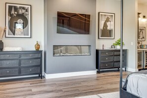 Ein modernes Schlafzimmer mit einem großen Bett, dunklem Holzboden und einem Kamin.