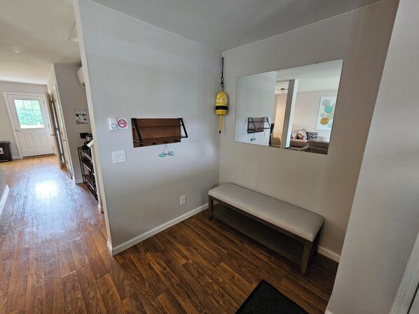 A hallway with a wooden floor, a bench, a wall-mounted shelf, a mirror, and a door. - Rent both apartments in a duplex. 6 bedrooms, 2 kitchens, 2 livings rooms. (Trenton)