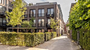 Ein modernes Apartmenthaus mit Balkonen, einem gepflasterten Weg und grünen Hecken.