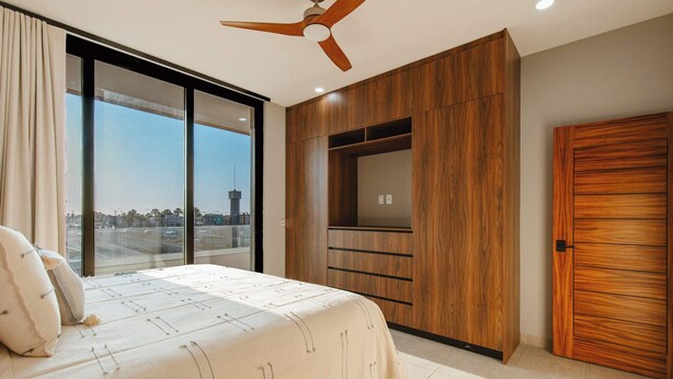 A bedroom with a bed, a ceiling fan, a large window, and a wardrobe. - Arch View Condo Cabo San Lucas • Panoramic Ocean Views | Suite 103 (Cabo San Lucas)