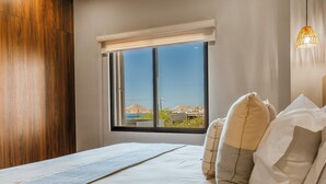 A bedroom with a large window, a bed with pillows, and a wooden panel on the wall. - Arch View Master Bedroom Condo Cabo San Lucas • Rooftop Infinity Pool | 101 (Cabo San Lucas)