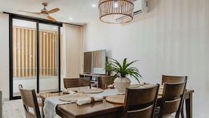 A dining area with a wooden table, six chairs, a ceiling fan, a large potted plant, and a television on the wall. - Arch View Master Bedroom Condo Cabo San Lucas • Rooftop Infinity Pool | 101 (Cabo San Lucas)