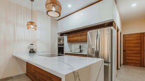 A modern kitchen with a marble island, stainless steel appliances, wooden accents, and pendant lighting. - Arch View Master Bedroom Condo Cabo San Lucas • Rooftop Infinity Pool | 101 (Cabo San Lucas)