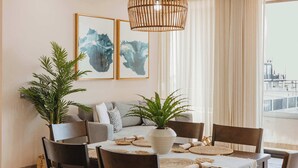 A dining area with a round table, chairs, and a ceiling fan. There are two framed artworks on the wall and a plant on the table. - Arch View Condo Cabo San Lucas • 2nd Floor | Rooftop Pool | 203 (Cabo San Lucas)