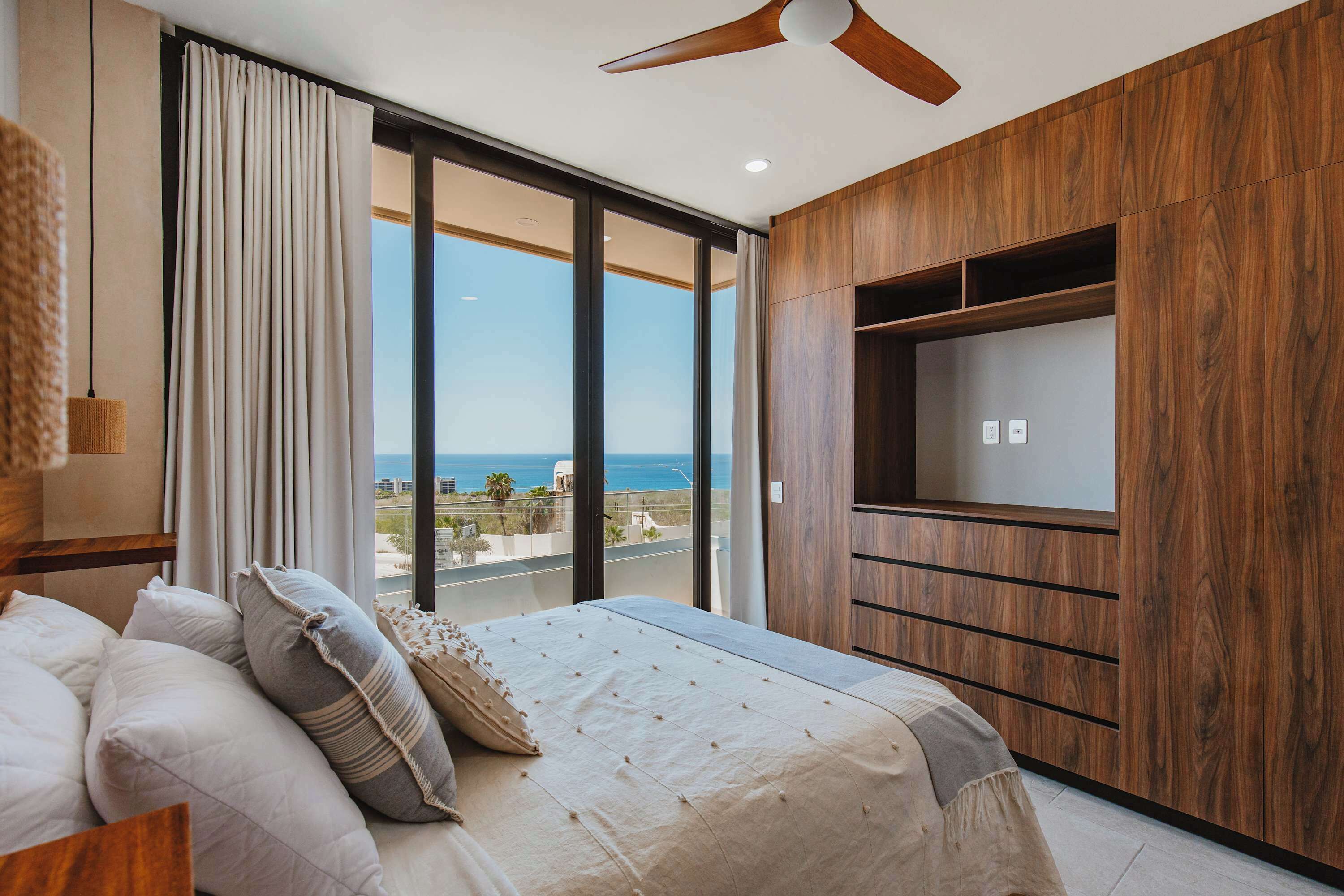 A bedroom with a large bed, a TV mounted on the wall, and a view of the sea.