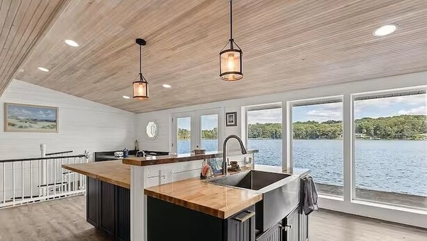 Una cocina moderna con una isla de madera, ventanas amplias y vistas a un lago.