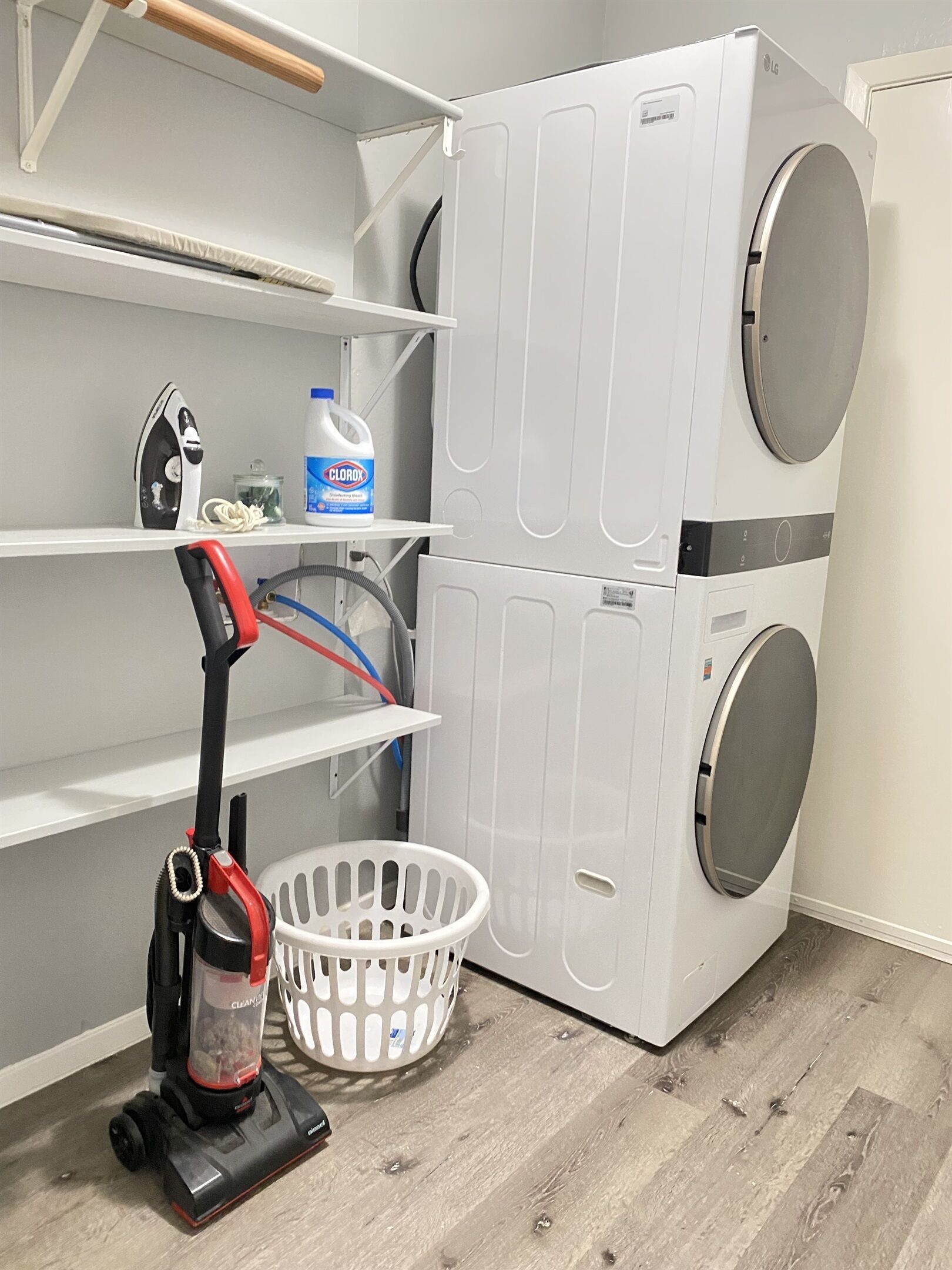 A laundry room with stacked washers and dryers, a vacuum cleaner, and a basket.