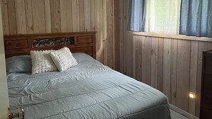 A bedroom with wooden panel walls, a bed with a headboard, and a window with curtains. - Classic Cottage Charm - relaxing & private.  #1 (Battersea)
