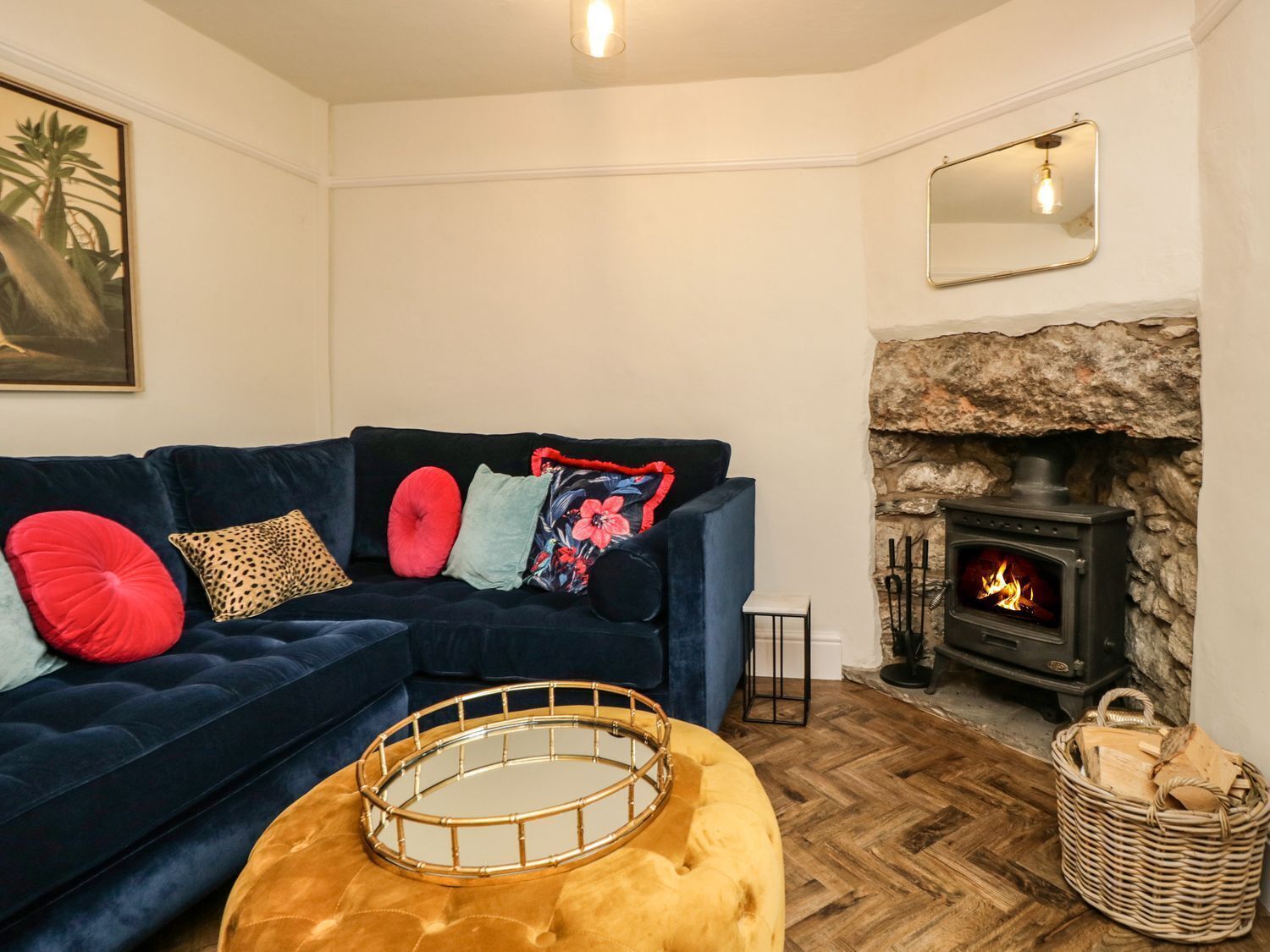 Un salon chaleureux avec un canapé bleu foncé, un pouf rond en bois, une cheminée en pierre et un miroir encadré accroché au mur.