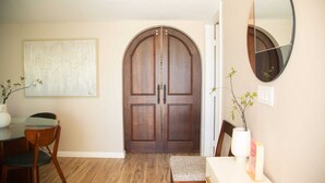 Ein Essbereich mit Holztisch, Stühlen und einer Bank. Eine große Holztür und ein Spiegel sind an der Wand angebracht.