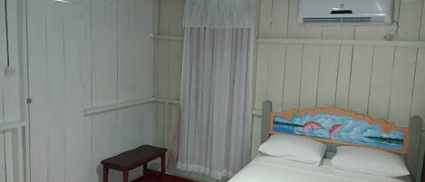 A hotel room with a bed, a bench, a toilet, and an air conditioning unit.