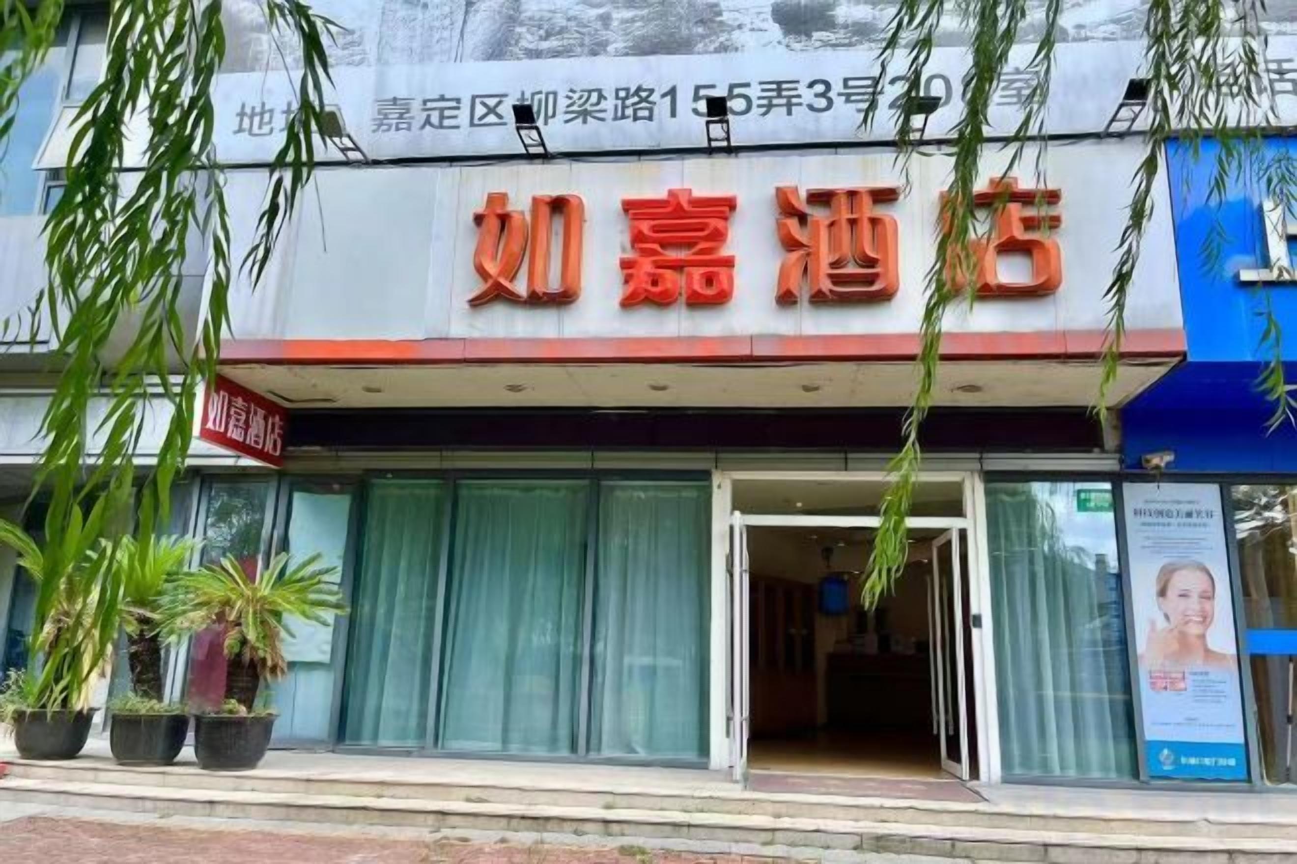 A hotel entrance with a signboard, potted plants, and a visible entrance door.