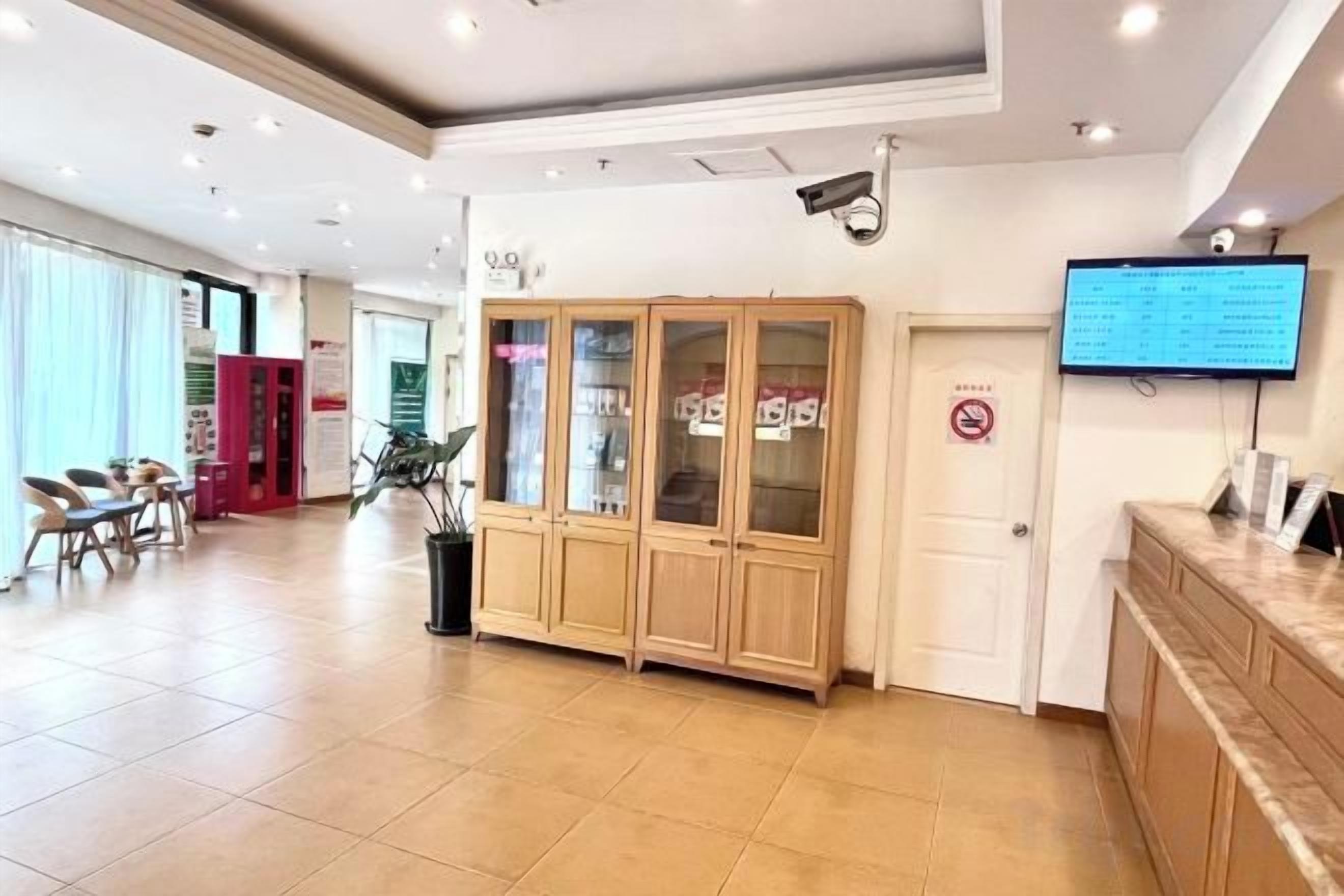 A hotel reception area with a reception desk, a digital screen, and a seating area with chairs.