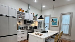 Een moderne keuken met witte kasten, een centraal eiland en een eethoek met rieten stoelen.
