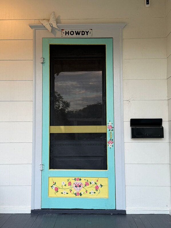 Una puerta turquesa con una sección inferior amarilla adornada con diseños florales, un letrero encima que dice “HOWDY” y un buzón a la derecha.