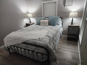 Una cama bien hecha con edredón blanco y almohada decorativa, dos lámparas de noche y una mesita de noche.