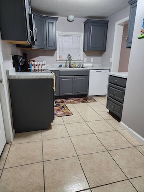 Una cocina compacta con gabinetes grises, una encimera blanca y un suelo de baldosas.