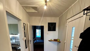Een gang met houten vloer, een plafondlamp, een deur met raam en een wandplank met een foto.
