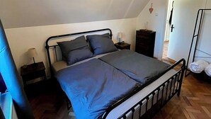 Een slaapkamer met een metalen bedframe, een houten plafondventilator, een nachtkastje en een bijzettafeltje.