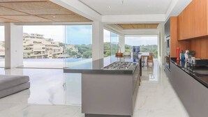Une cuisine moderne dotée d’un îlot central, de grandes fenêtres offrant une vue sur la ville, et d’un coin repas avec une table et des chaises.