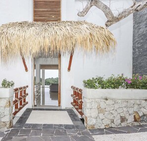 A building entrance with a thatched roof, stone walls, and a view of the landscape.