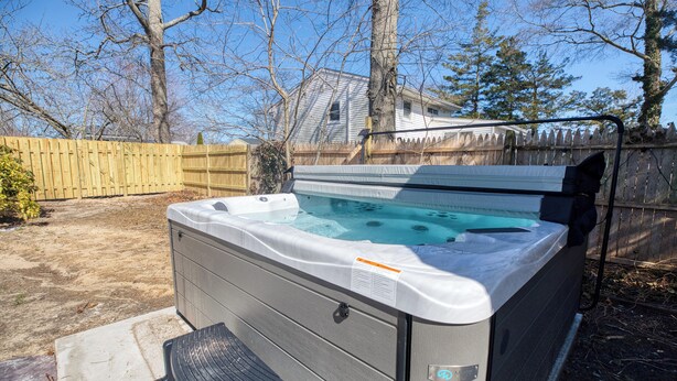 Ein Whirlpool in einem Garten mit Holzzaun, einem Haus im Hintergrund und kahl stehenden Bäumen.