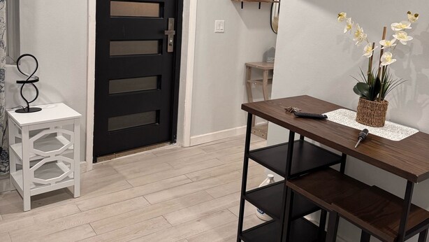 A modern room with a black door, a TV mounted on the wall, a small table with a plant, and a white side table with a decorative item.