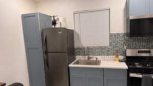 A compact kitchen with grey cabinets, a stainless steel refrigerator, a microwave, and a stove.