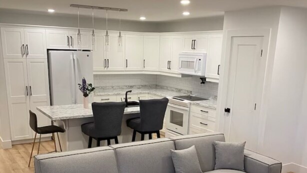 Een moderne woonkamer met een grijze hoekbank, een houten salontafel en een keuken met witte kasten en een magnetron.