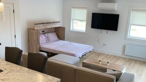 Een moderne, compacte woonruimte met een slaapbank, een eettafel en een aan de muur bevestigde televisie.